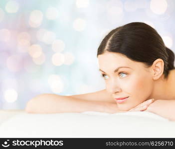 people, beauty, holidays and body care concept - happy beautiful woman lying on massage desk at spa over blue lights background