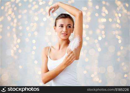 people, beauty, hygiene, depilation and epilation concept - beautiful woman sitting on bed and touching her armpit with feather at home bedroom. woman with feather touching her armpit at home
