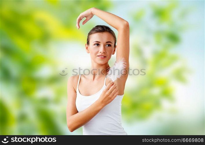 people, beauty, hygiene, depilation and epilation concept - beautiful woman touching her armpit by feather over green natural background. beautiful woman touching her armpit by feather. beautiful woman touching her armpit by feather