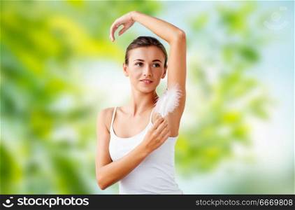 people, beauty, hygiene, depilation and epilation concept - beautiful woman touching her armpit by feather over green natural background. beautiful woman touching her armpit by feather. beautiful woman touching her armpit by feather