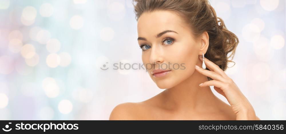 people, beauty, jewelry and accessories concept - beautiful woman with diamond earrings over blue holidays lights background