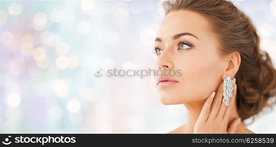 people, beauty, jewelry and accessories concept - beautiful woman with diamond earrings over blue holidays lights background