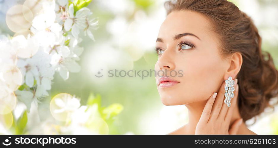 people, beauty, jewelry and accessories concept - beautiful woman with diamond earrings over summer garden and cherry blossom background