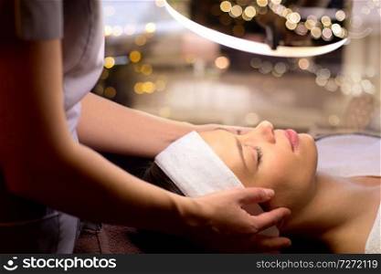 people, beauty, lifestyle and relaxation concept - beautician with magnifying l&doing face massage to beautiful young woman at spa. beautician doing face massage to woman at spa