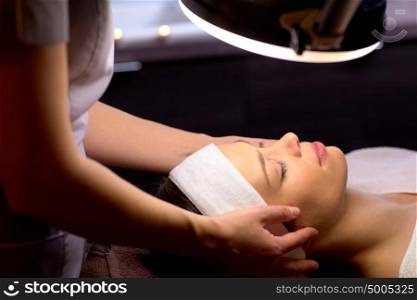 people, beauty, lifestyle and relaxation concept - beautician with magnifying lamp doing face massage to beautiful young woman at spa. beautician doing face massage to woman at spa