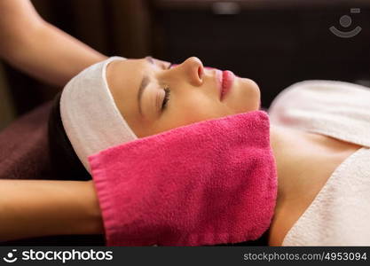 people, beauty, lifestyle and relaxation concept - beautiful young woman lying with closed eyes and having face massage with terry gloves at spa. woman having face massage with terry gloves at spa