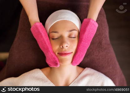 people, beauty, lifestyle and relaxation concept - beautiful young woman lying with closed eyes and having face massage with terry gloves at spa. woman having face massage with terry gloves at spa