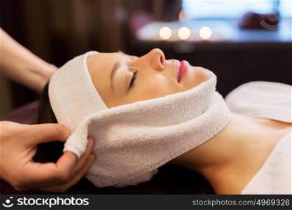 people, beauty, lifestyle and relaxation concept - beautiful young woman lying with closed eyes and having face massage with towel at spa. woman having face massage with towel at spa