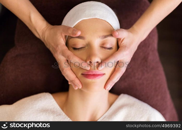 people, beauty, lifestyle and relaxation concept - beautiful young woman lying with closed eyes and having face and head massage at spa. woman having face and head massage at spa