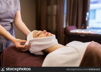 people, beauty, lifestyle and relaxation concept - beautiful young woman lying with closed eyes and having face massage with towel at spa parlor. woman having face massage with towel at spa parlor