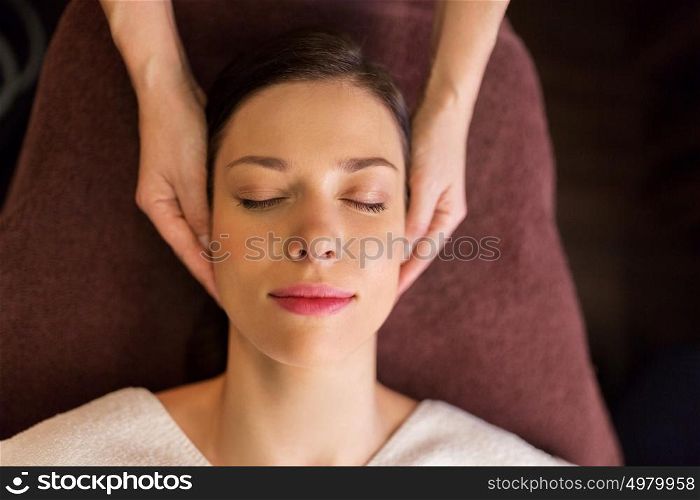 people, beauty, lifestyle and relaxation concept - beautiful young woman lying with closed eyes and having face and head massage at spa. woman having face and head massage at spa