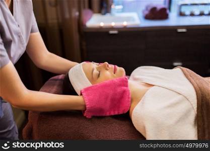 people, beauty, lifestyle and relaxation concept - beautiful young woman lying with closed eyes and having face massage with terry gloves at spa parlor. woman having face massage with terry gloves at spa