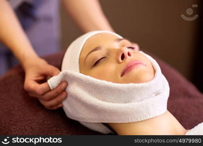 people, beauty, lifestyle and relaxation concept - beautiful young woman lying with closed eyes and having face massage with towel at spa. woman having face massage with towel at spa