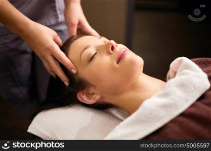 people, beauty, lifestyle and relaxation concept - beautiful young woman lying with closed eyes and having head massage at spa. woman having head massage at spa