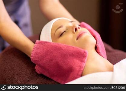 people, beauty, lifestyle and relaxation concept - beautiful young woman lying with closed eyes and having face massage with terry gloves at spa. woman having face massage with terry gloves at spa