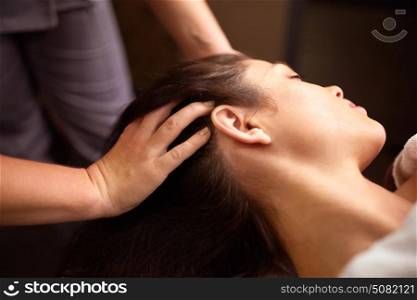 people, beauty, lifestyle and relaxation concept - beautiful young woman lying with closed eyes and having head massage at spa. woman having head massage at spa