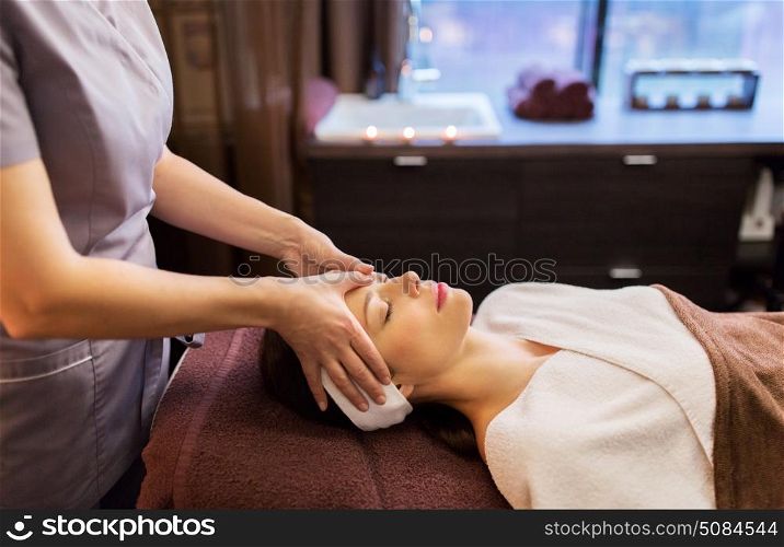 people, beauty, lifestyle and relaxation concept - beautiful young woman lying with closed eyes and having face and head massage at spa parlor. woman having face and head massage at spa parlor. woman having face and head massage at spa parlor