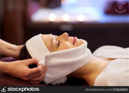 people, beauty, lifestyle and relaxation concept - beautiful young woman lying with closed eyes and having face massage with towel at spa. woman having face massage with towel at spa. woman having face massage with towel at spa