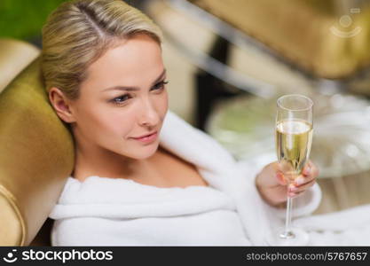 people, beauty, lifestyle, holidays and relaxation concept - beautiful young woman in white bath robe lying on chaise-longue and drinking champagne at spa