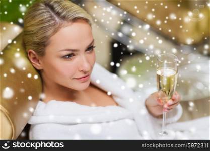 people, beauty, lifestyle, holidays and relaxation concept - beautiful young woman in white bath robe lying on chaise-longue and drinking champagne at spa with snow effect