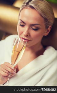 people, beauty, lifestyle, holidays and relaxation concept - beautiful young woman in white bath robe drinking champagne at spa