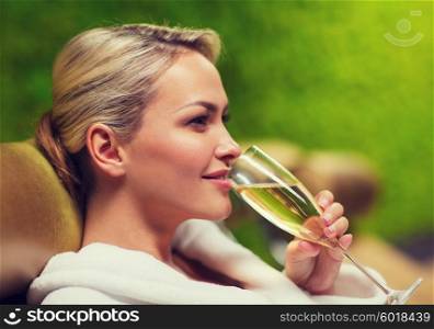 people, beauty, lifestyle, holidays and relaxation concept - beautiful young woman in white bath robe lying on chaise-longue and drinking champagne at spa