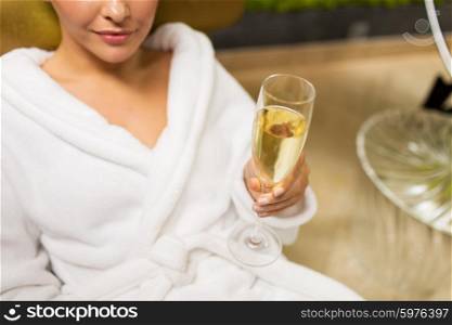 people, beauty, lifestyle, holidays and relaxation concept - close up of beautiful young woman in white bath robe lying on chaise-longue and drinking champagne at spa