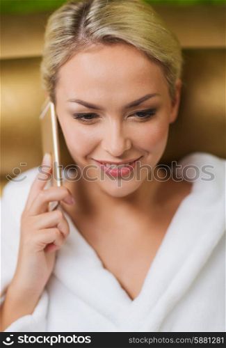 people, beauty, lifestyle, technology and relaxation concept - beautiful young woman in white bath robe with smartphone calling and talking at spa