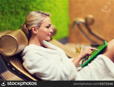 people, beauty, lifestyle, technology and relaxation concept - beautiful young woman in white bath robe with tablet pc computer social networking at spa