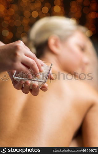 people, beauty, massage and relaxation concept - close up of young woman lying and therapist holding salt bowl in spa