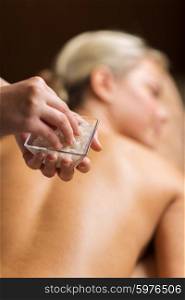 people, beauty, massage and relaxation concept - close up of young woman lying and therapist holding salt bowl in spa