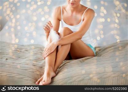 people, beauty, skincare and bodycare concept - beautiful woman sitting on bed and touching hand skin with feather at home bedroom. woman with feather touching her hand skin on bed