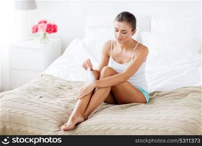 people, beauty, skincare and bodycare concept - beautiful woman sitting on bed and touching hand skin with feather at home bedroom. woman with feather touching her hand skin on bed