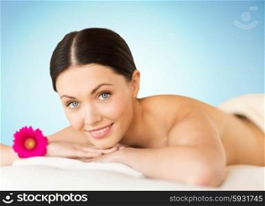 people, beauty, spa and body care concept - happy beautiful woman lying on massage desk at spa over blue background