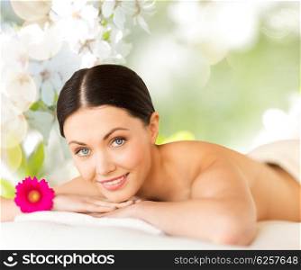 people, beauty, spa and body care concept - happy beautiful woman lying on massage desk over green natural cherry blossom background