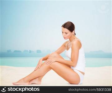 people, beauty, spa and resort concept - beautiful woman in cotton underwear touching her legs over infinity edge pool background