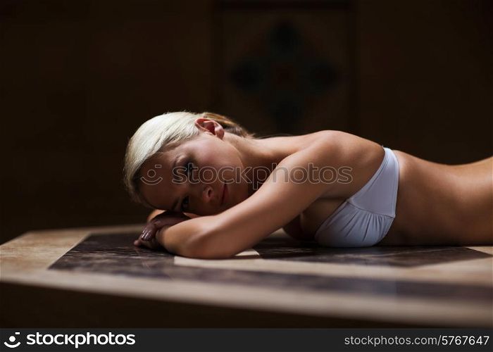people, beauty, spa, healthy lifestyle and relaxation concept - beautiful young woman lying on hammam table in turkish bath