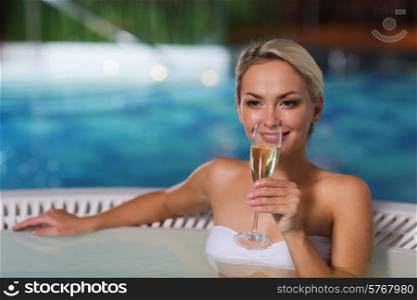 people, beauty, spa, healthy lifestyle and relaxation concept - beautiful young woman wearing bikini swimsuit sitting with glass of champagne in jacuzzi at poolside