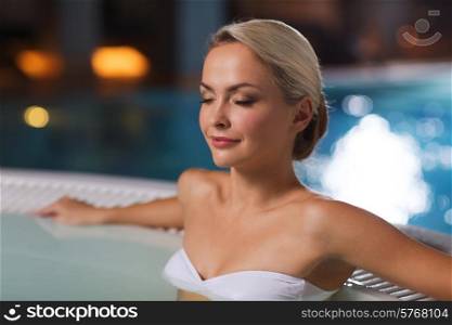 people, beauty, spa, healthy lifestyle and relaxation concept - beautiful young woman wearing bikini swimsuit sitting in jacuzzi at poolside