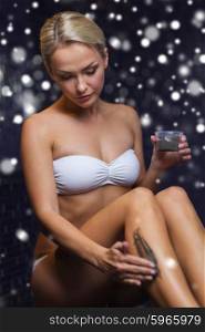 people, beauty, spa, healthy lifestyle and relaxation concept - beautiful young woman in swimsuit applying therapeutic mud in bath or sauna with snow effect