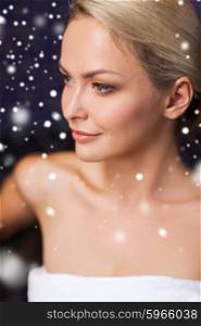 people, beauty, spa, healthy lifestyle and relaxation concept - beautiful young woman sitting in bath towel at sauna with snow effect