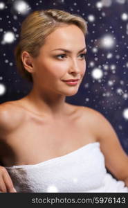 people, beauty, spa, healthy lifestyle and relaxation concept - beautiful young woman sitting in bath towel at sauna with snow effect