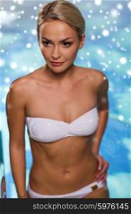 people, beauty, spa, healthy lifestyle and relaxation concept - beautiful young woman in bikini swimsuit raising upstairs in swimming pool with snow effect