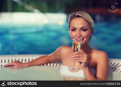 people, beauty, spa, healthy lifestyle and relaxation concept - beautiful young woman wearing bikini swimsuit sitting with glass of champagne in jacuzzi at poolside