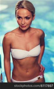 people, beauty, spa, healthy lifestyle and relaxation concept - beautiful young woman in bikini swimsuit raising upstairs in swimming pool