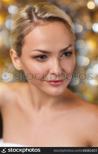 people, beauty, spa, healthy lifestyle and relaxation concept - close up of beautiful young woman sitting in bath towel over holidays lights background