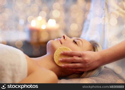 people, beauty, spa, healthy lifestyle and relaxation concept - close up of beautiful young woman lying with closed eyes and having face massage with sponge in spa