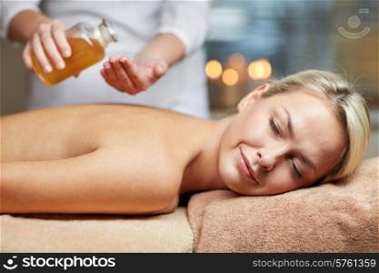 people, beauty, spa, healthy lifestyle and relaxation concept - close up of beautiful young woman lying with closed eyes on massage table and therapist holding oil bottle in spa