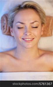 people, beauty, spa, healthy lifestyle and relaxation concept - close up of beautiful smiling young woman lying with closed eyes in spa