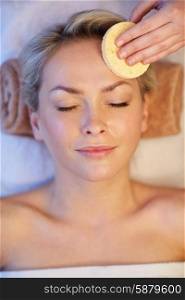 people, beauty, spa, healthy lifestyle and relaxation concept - close up of beautiful young woman lying with closed eyes and having face massage with sponge in spa